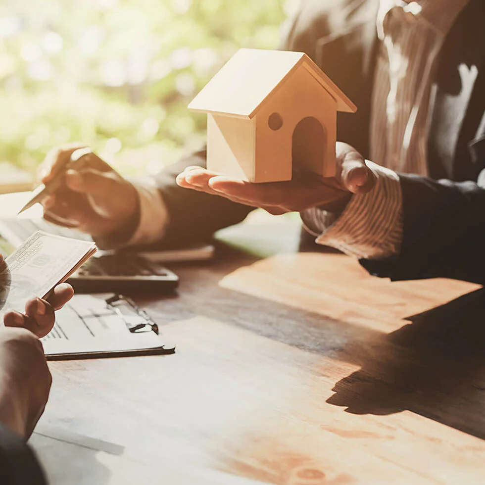 A small model house held in two hands over a desk